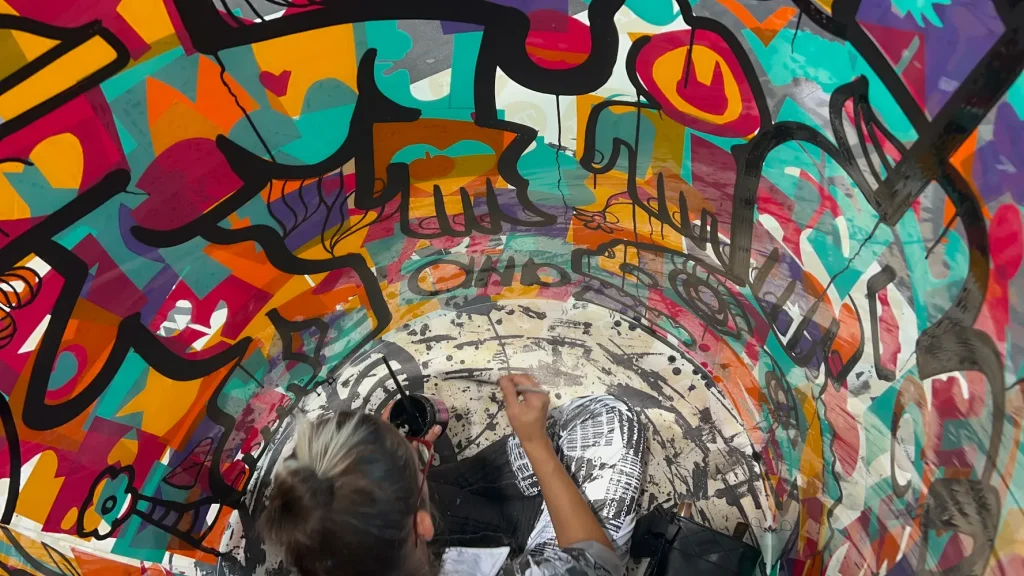 L'artiste aNa peignant en direct à l'intérieur d'un tube transparent couvert de graffitis colorés lors d'une performance d'art urbain à Bordeaux.