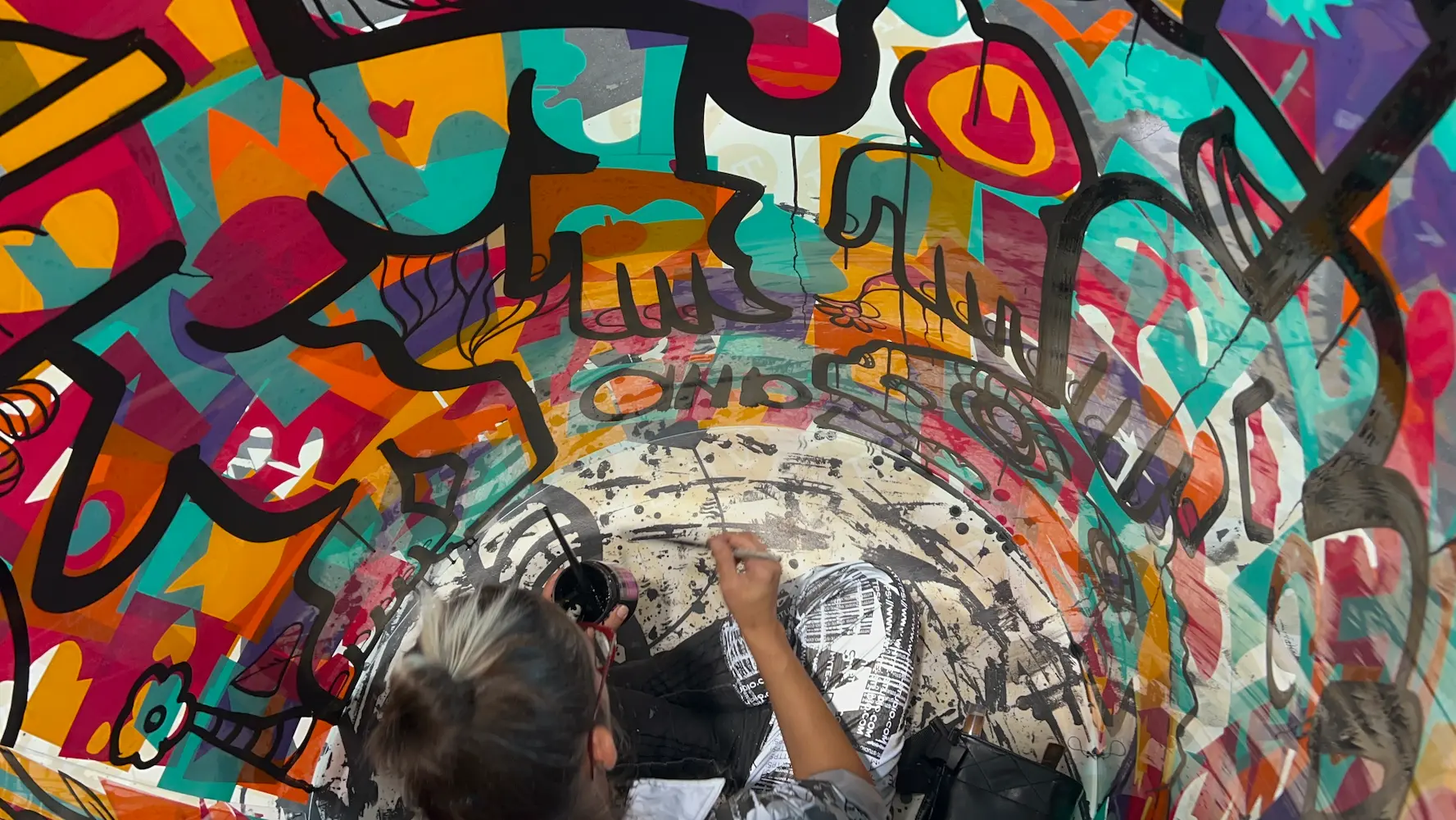 L'artiste aNa peignant en direct à l'intérieur d'un tube transparent couvert de graffitis colorés lors d'une performance d'art urbain à Bordeaux.